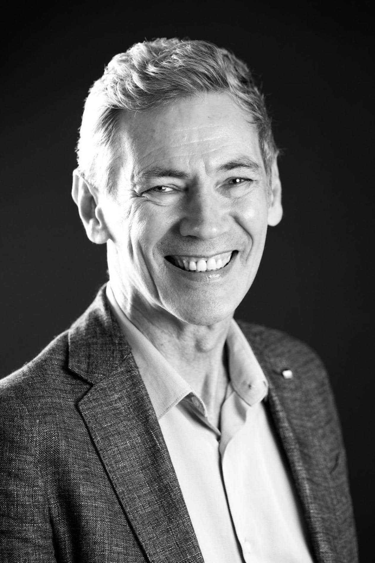 Portrait noir et blanc d'un membre de l'équipe souriant en veste grise et chemise blanche